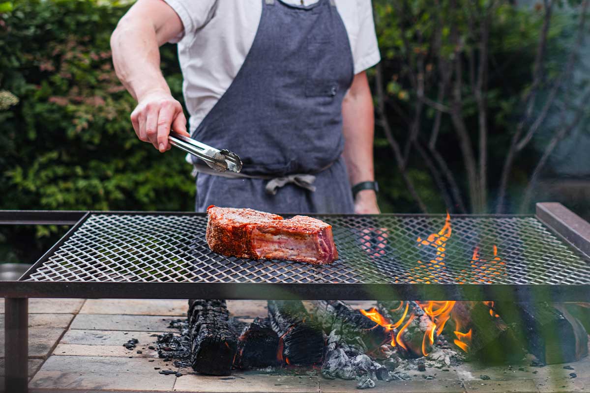 man grilling steak on open fire grill