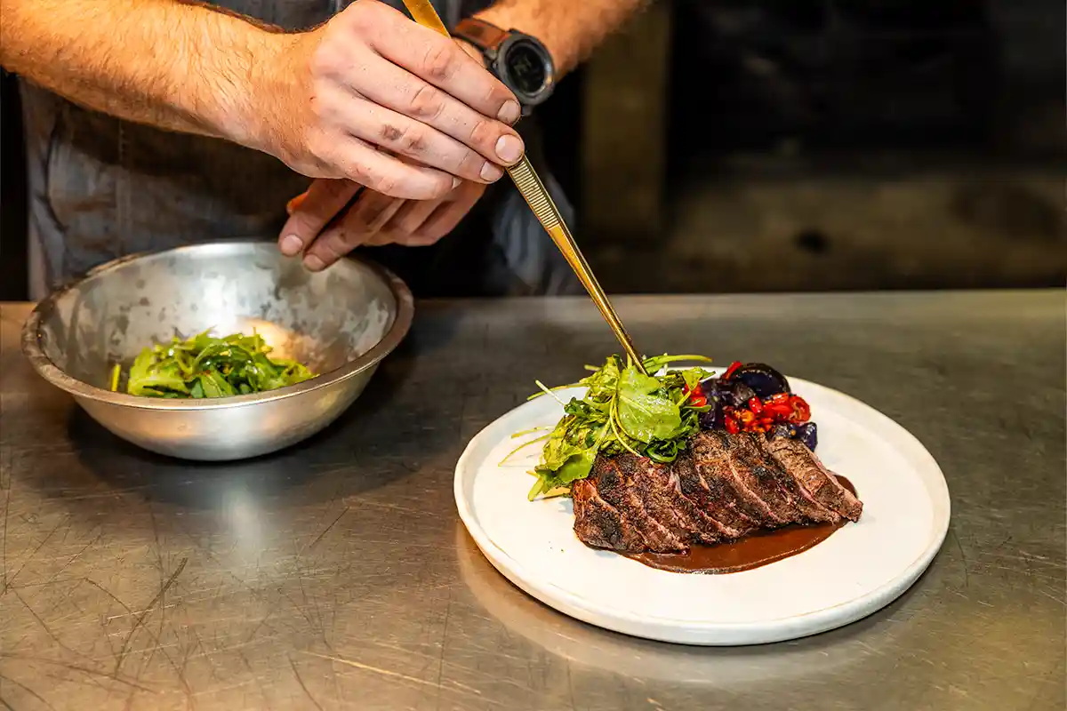 chef plating greens on top of steak
