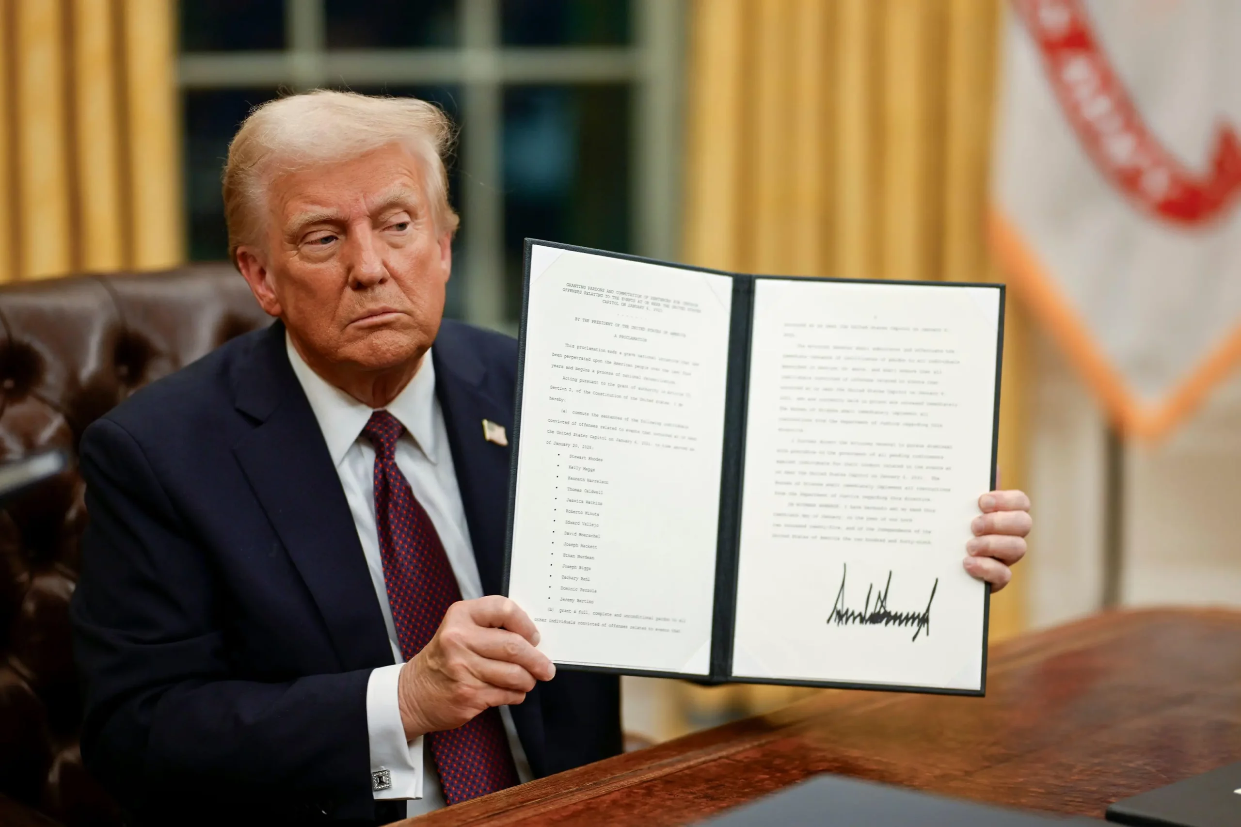 Donald Trump in the Oval Office holding up an executive order