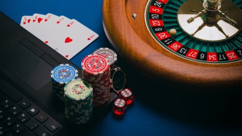 gambling image of playing cards, chips and a roulette wheel on brown wooden table