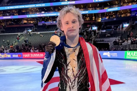 Figure Skater Ilia Malinin wears a U.S. flag and holds his medal on the ice after winning the 2025 ISU World Figure Skating Championships