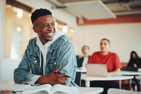 student sitting at a desk with book open smiling