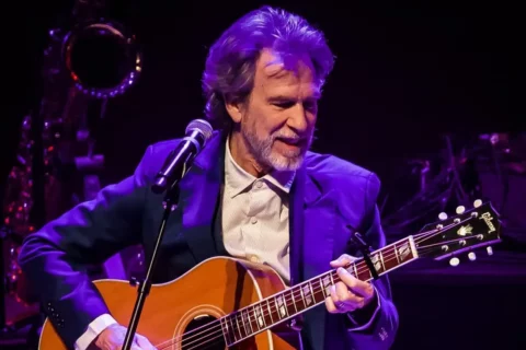 Jon Carroll holds a guitar singing in front of a microphone
