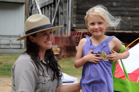 A NPS park ranger with a young girl who is putting a junior ranger badge on her shirt for Junior Ranger Day
