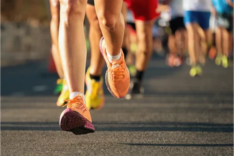a person in orange running shoes running on a road ahead of other runners