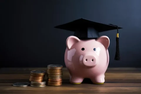 piggy bank wearing grad cap next to stacks of coins