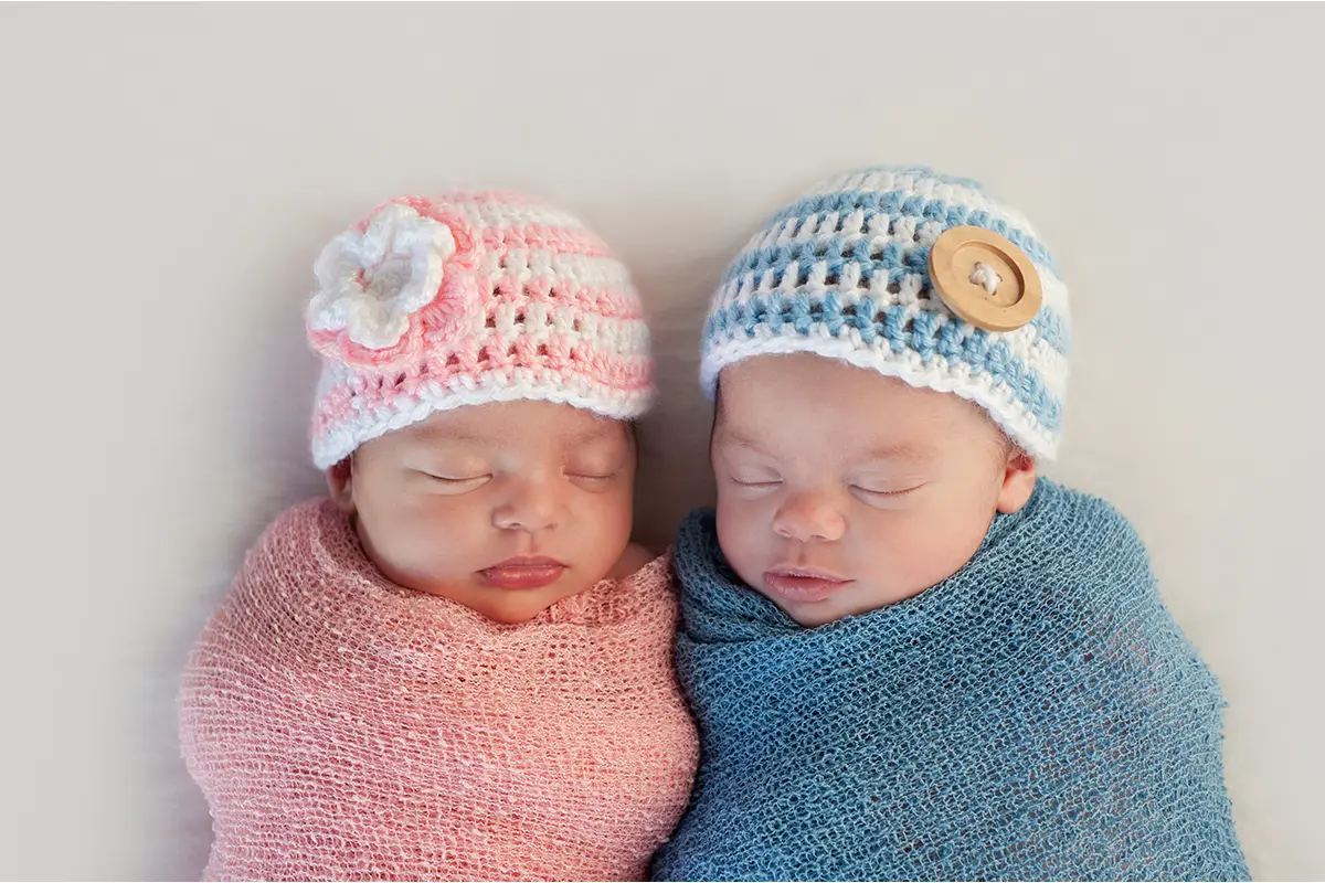 a baby sleeping in a pink hat and blanket beside a baby sleeping in a blue hat and blanket