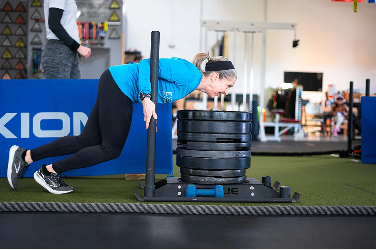A woman pushes weights along a track during Hyrox training