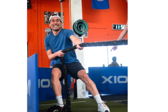 A man pulls on a rope in a gym during Hyrox training