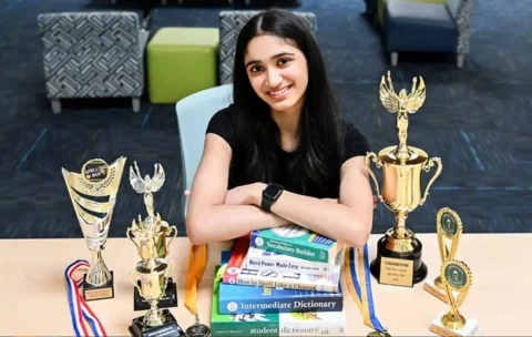 FCPS student Nikita Ramakrishnan sits with books and spelling bee trophies