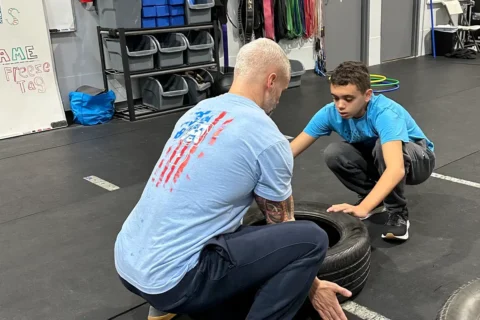 CrossFit Coach Chad Ciri helps his son push a tire in a uniquely abled fitness class