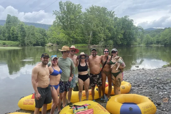 A group of people stand by the river with water tubes on the ground