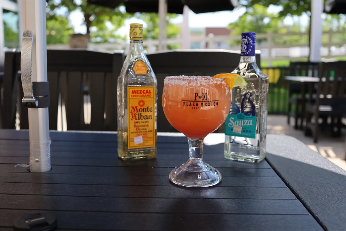 A bottle of tequila and a marguerita sit on an outdoor patio table at Plaza Mexico