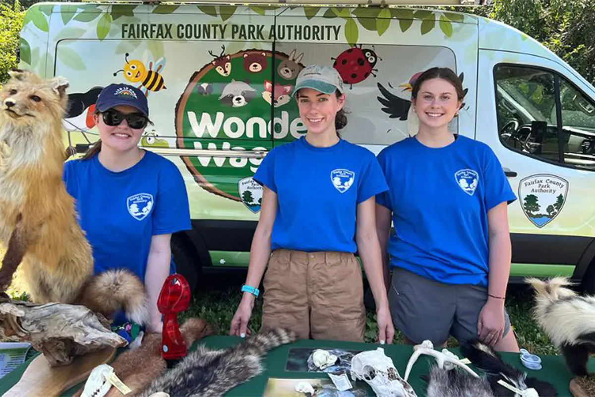 Three women in blue T-shirts stand in front of a Wonder Wagon van
