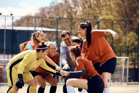 a group of adults outside on a field huddle up while playing soccer