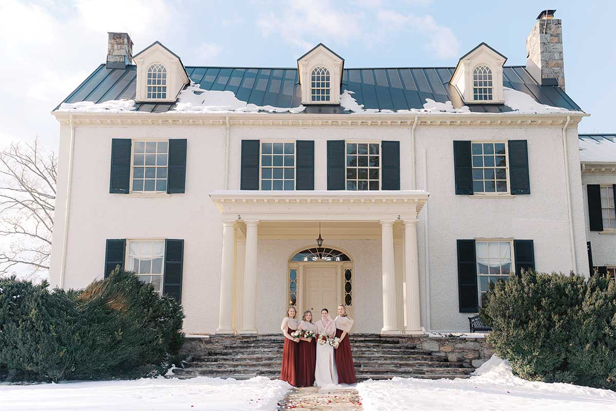 bride and bridesmaids standing in from of rust manor house