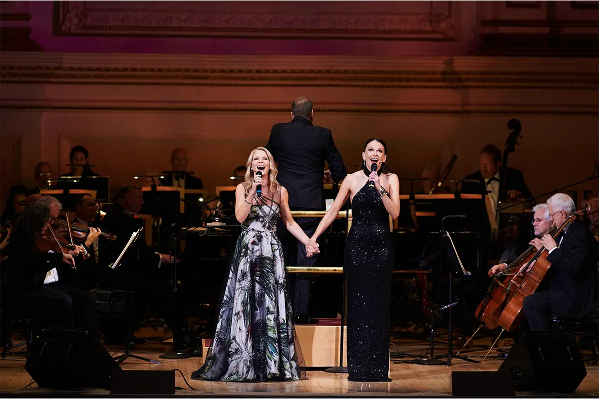 Kelli O'Hara and Sutton Foster holding hands singing on stage