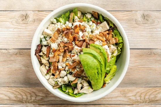 sliced avocado, greens and chicken in a round bowl on a table