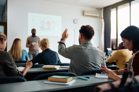 adults in a classroom with one person raising their hand
