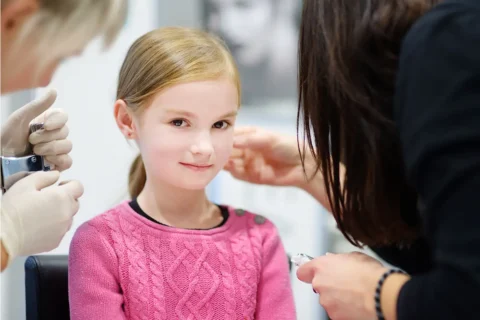 a young girl in a pink sweater getting her ears pierced