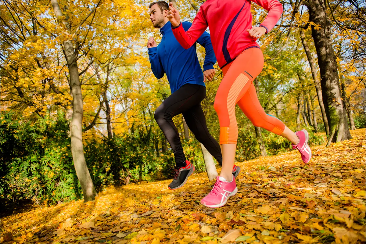 two people running with fall leaves and trees