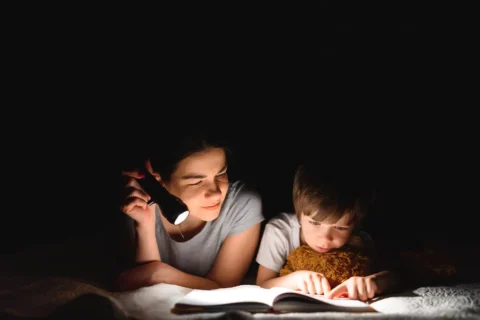 2 children read a book with a flashlight
