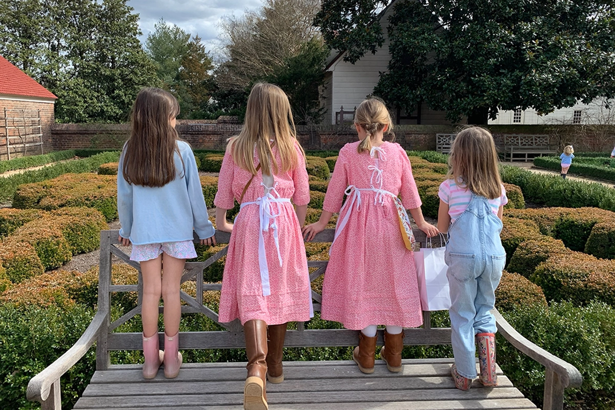 four girls standing on top of a bench looking at a garden