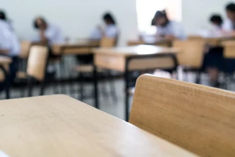 an empty desk and blurred image of kids in a school classroom
