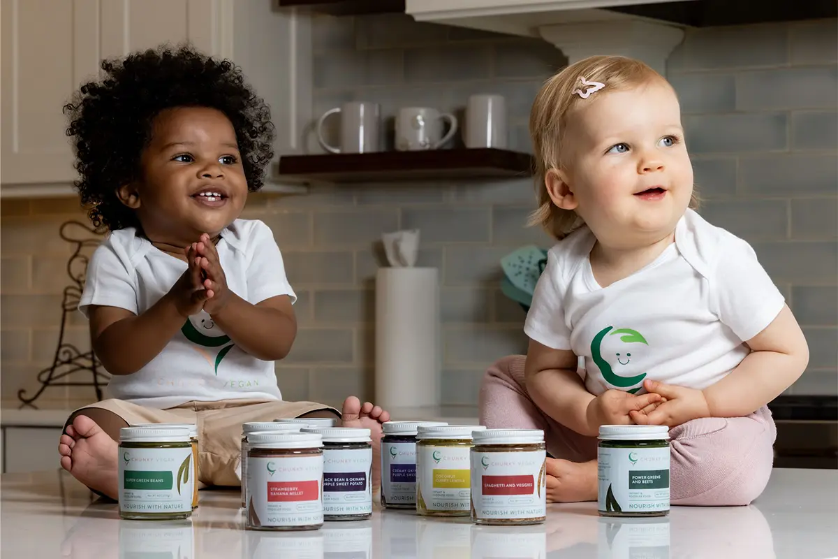 2 babies on a counter with jars of Chunky Vegan Baby Food