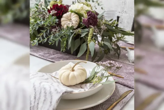 Table setting up-close with small white pumpkin on decorated plate and flower display in the center of the table