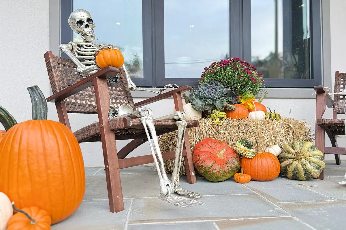 Fall decorations on front porch with fake skeleton sitting in chir