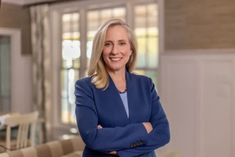 Abigail Spanberger stands smiling with her arms crossed wearing a blue blazer.