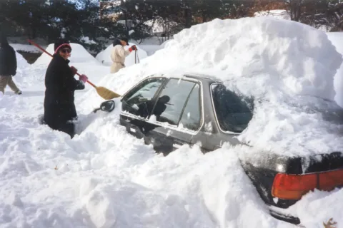 Woman shoveling snow off car