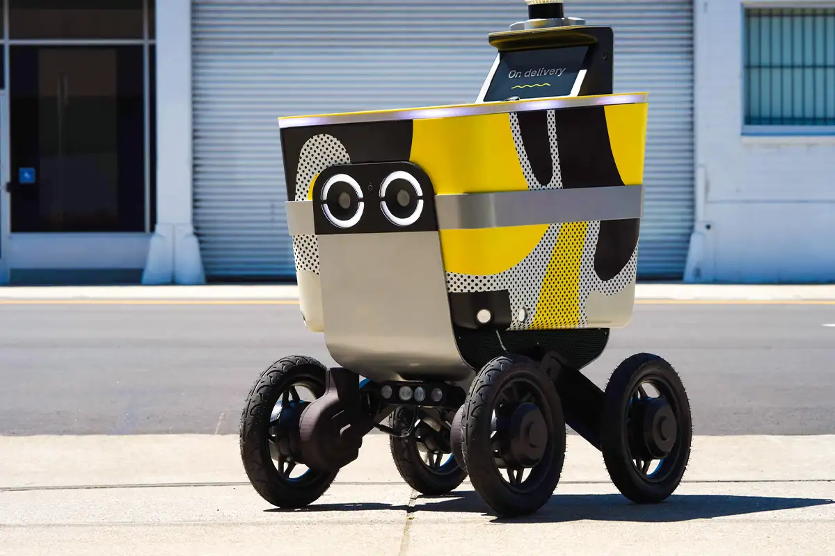 a yellow food delivery robot on a sidewalk