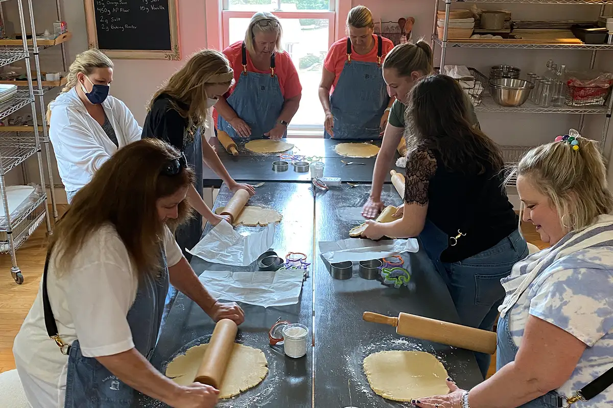 women stand around a table with rolling pics and dough at a baking workshop