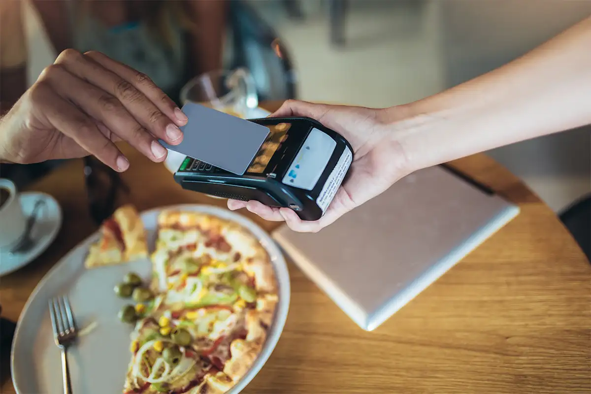 a person pays for their meal at a restaurant with pizza on the table