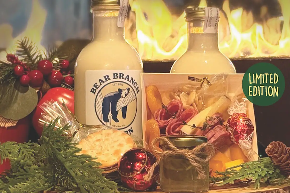 eggnog in glass pitchers on a charcuterie board with holiday ornaments and holly