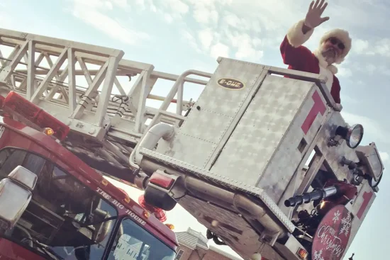 A man dressed as Santa waves atop a cherry picker in a fire truck