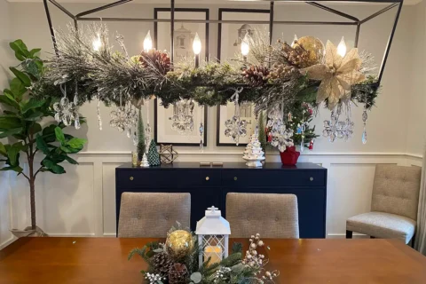 a dining room table with Christmas decorations on the chandelier and a centerpiece