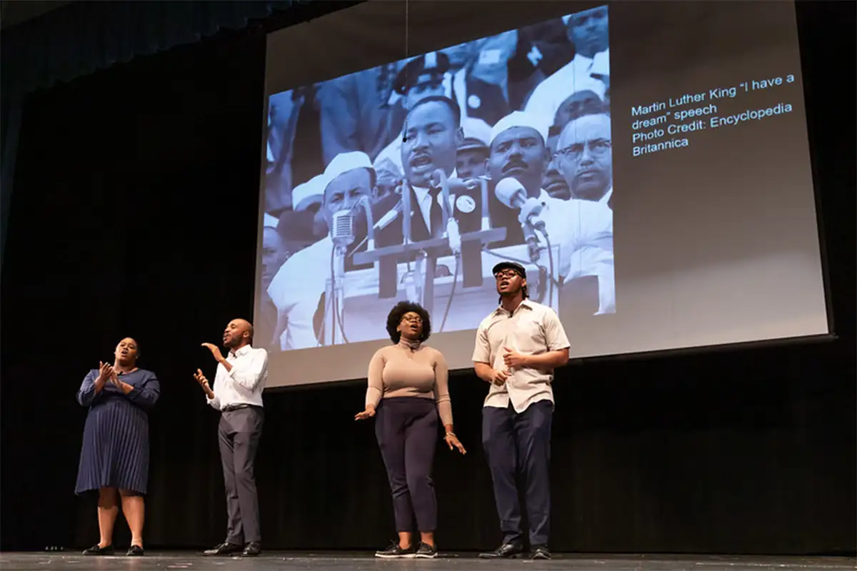 people stand on stage with images of Dr. Martin Luther King on a screen in the background