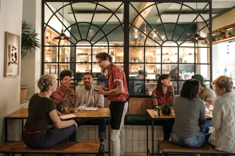 a waiter speaks to a group of people eating at a restaurant