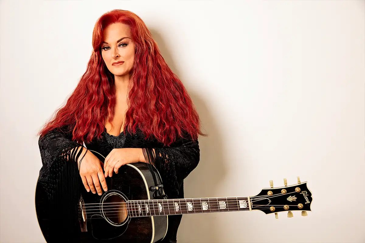 Wynonna Judd with her guitar lean on a white background