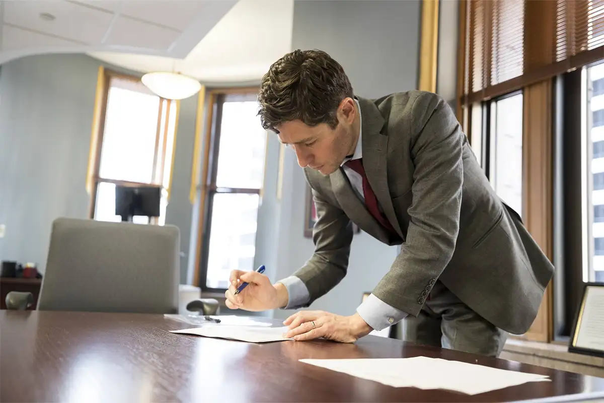 Minneapolis mayor Jacob Frey leans on desk over paperwork with a pen in hand