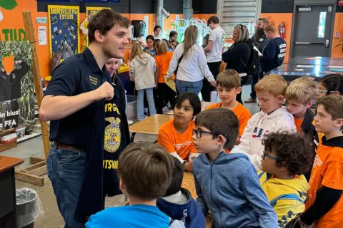 Hunter Ringer holds up his Future Farmers of America jacket while surrounded by elementary school students