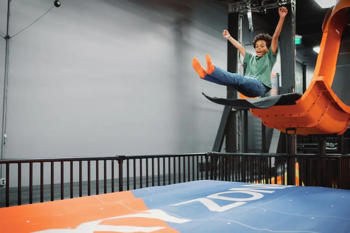 a young boy jumps from a slide onto a trampoline