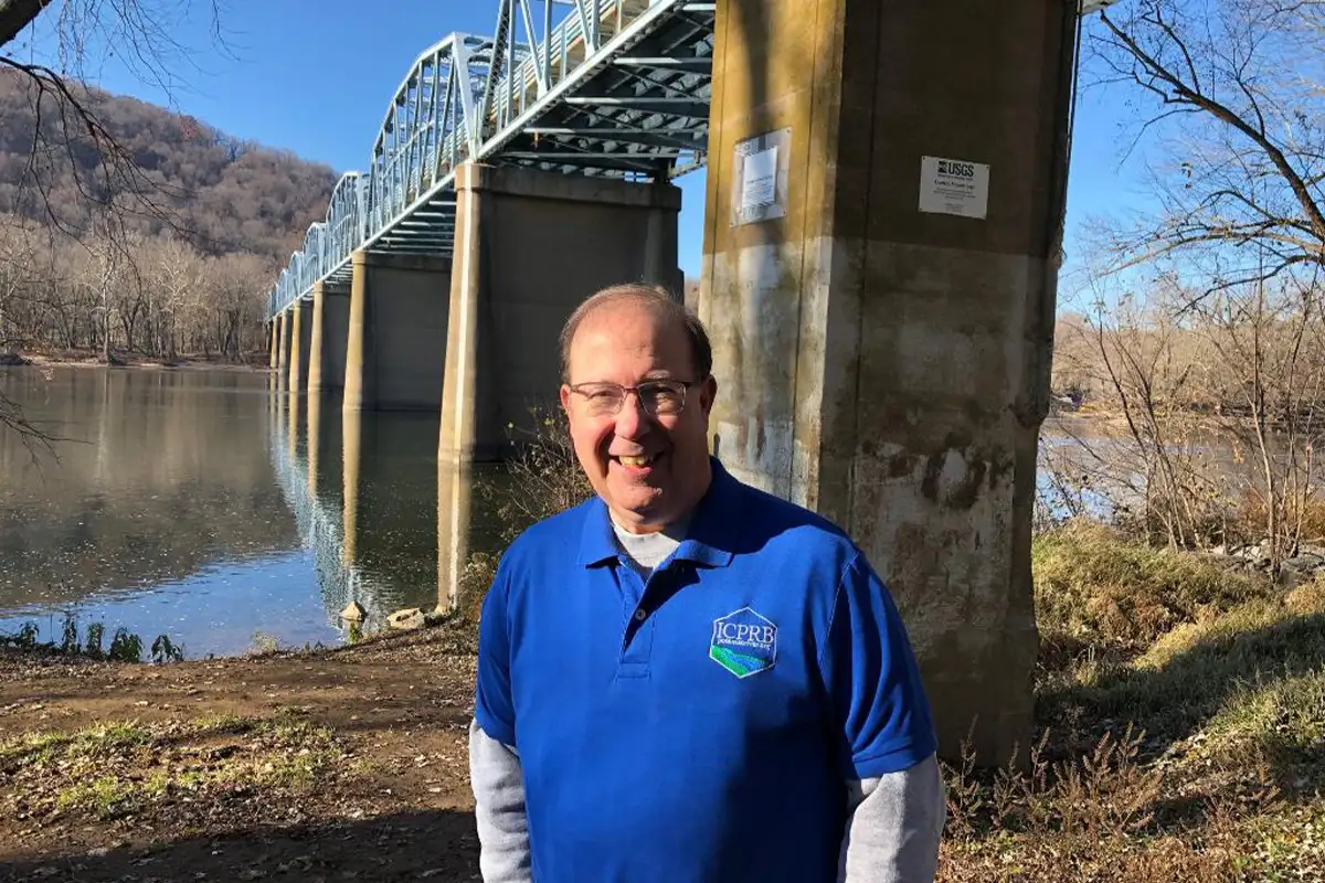 Arlington resident Michael Nardolilli in a blue shirt stands on the banks of the Potomac River