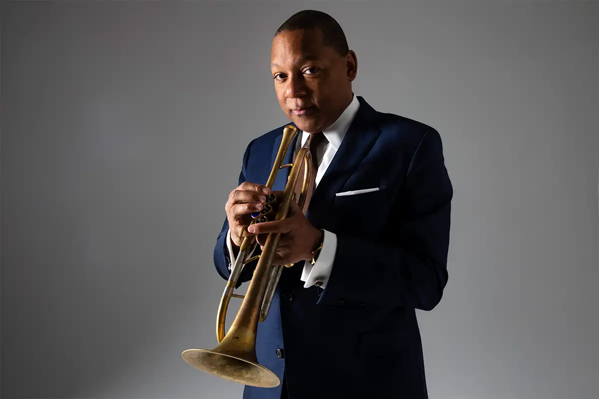 Wynton Marsalis holding a horned instrument in front of a gray background