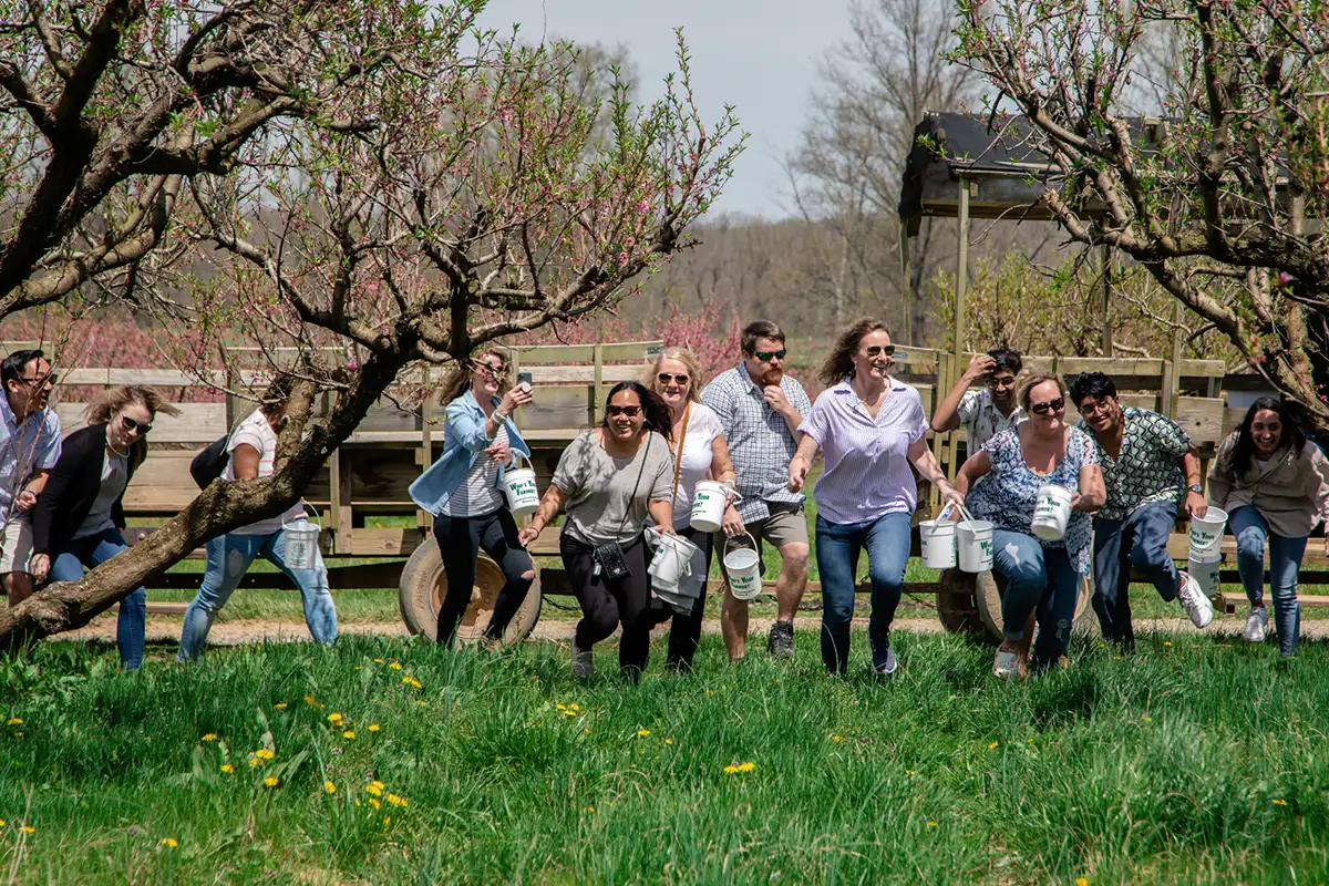 a group of adults holding buckets run into a grassy field