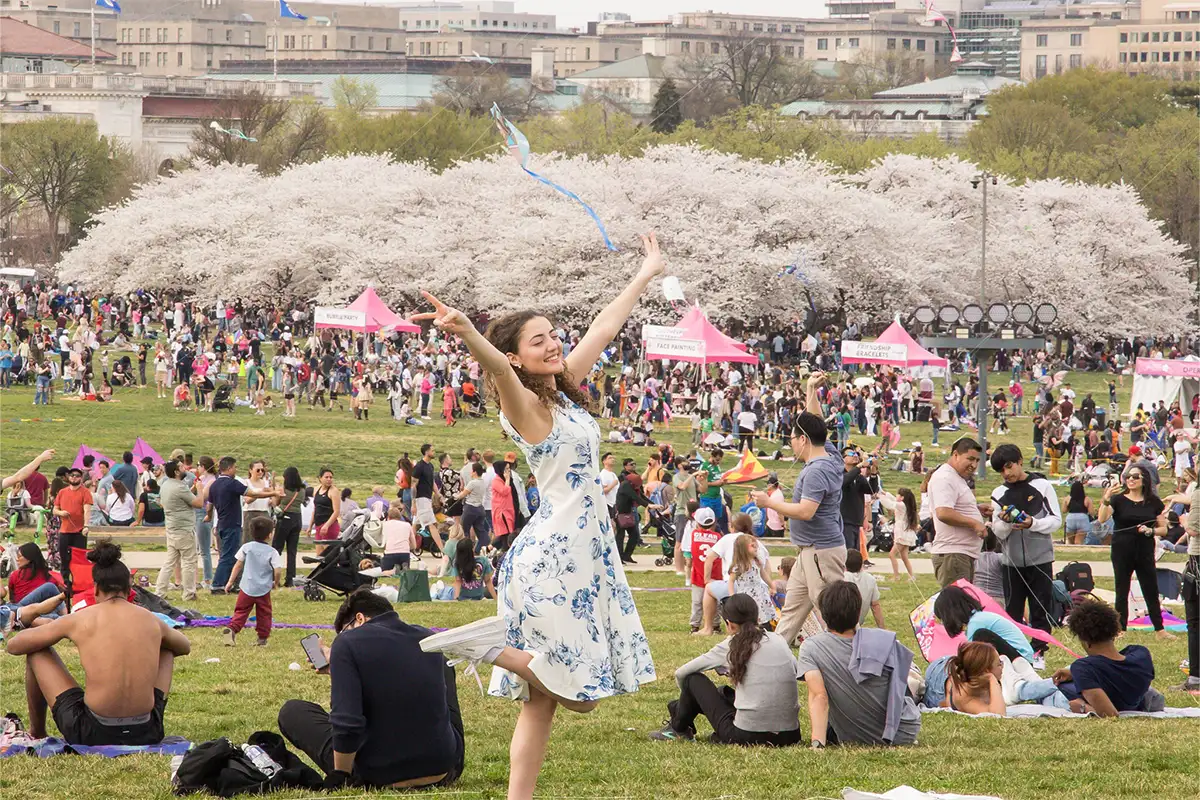 a girl reaches her arms to the sky with the cherry blossoms in the background