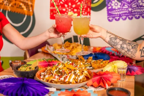 two people hold up colorful drinks over Mexican food at Austin Grill